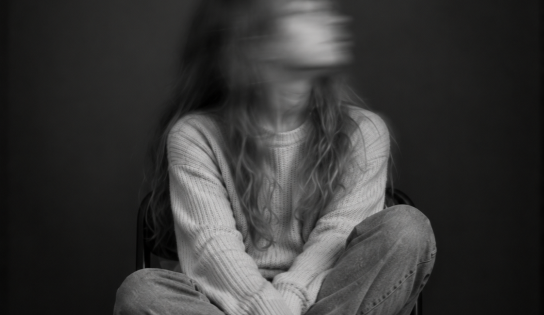 Sitzende Person mit langen Haaren und heller Kleidung, die mit gekreuzten Beinen auf einem Stuhl sitzt. Das nach oben gedrehte Gesicht ist durch Bewegungsunschärfe verschwommen.