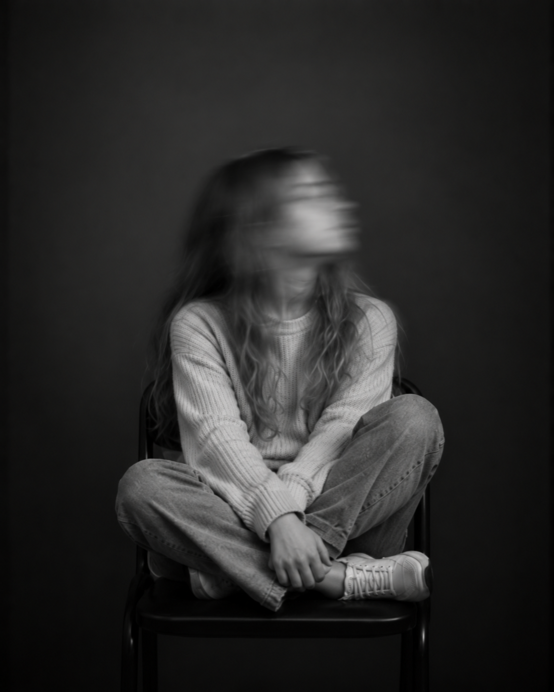 Sitzende Person mit langen Haaren und heller Kleidung, die mit gekreuzten Beinen auf einem Stuhl sitzt. Das nach oben gedrehte Gesicht ist durch Bewegungsunschärfe verschwommen.