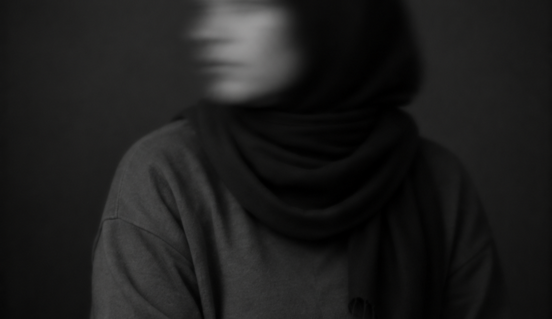 Sitzende Frau in dunkler Kleidung, deren zur Seite gedrehtes Gesicht durch Bewegungsunschärfe verschwommen ist.