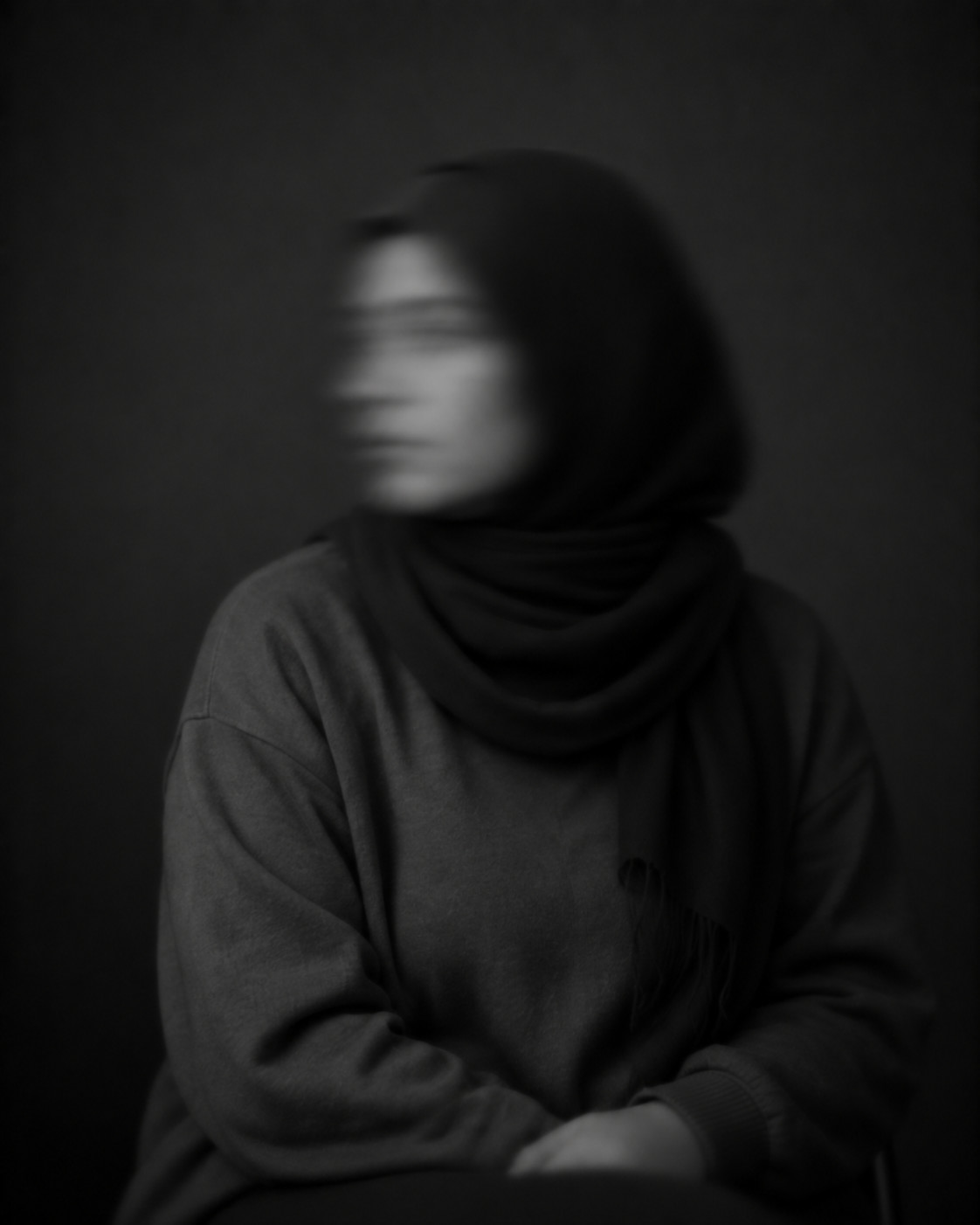 Sitzende Frau in dunkler Kleidung, deren zur Seite gedrehtes Gesicht durch Bewegungsunschärfe verschwommen ist.