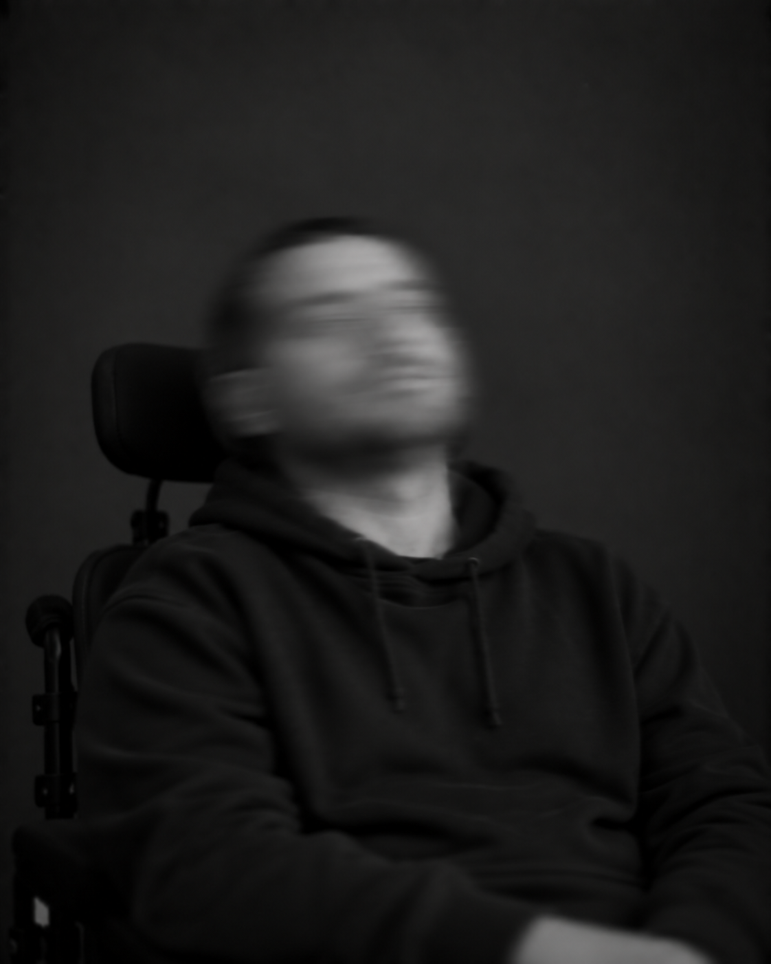 Sitzende Person in dunkler Kleidung mit Kopfstütze. Der nach oben und zur Seite gedrehte Kopf ist durch Bewegungsunschärfe verschwommen.