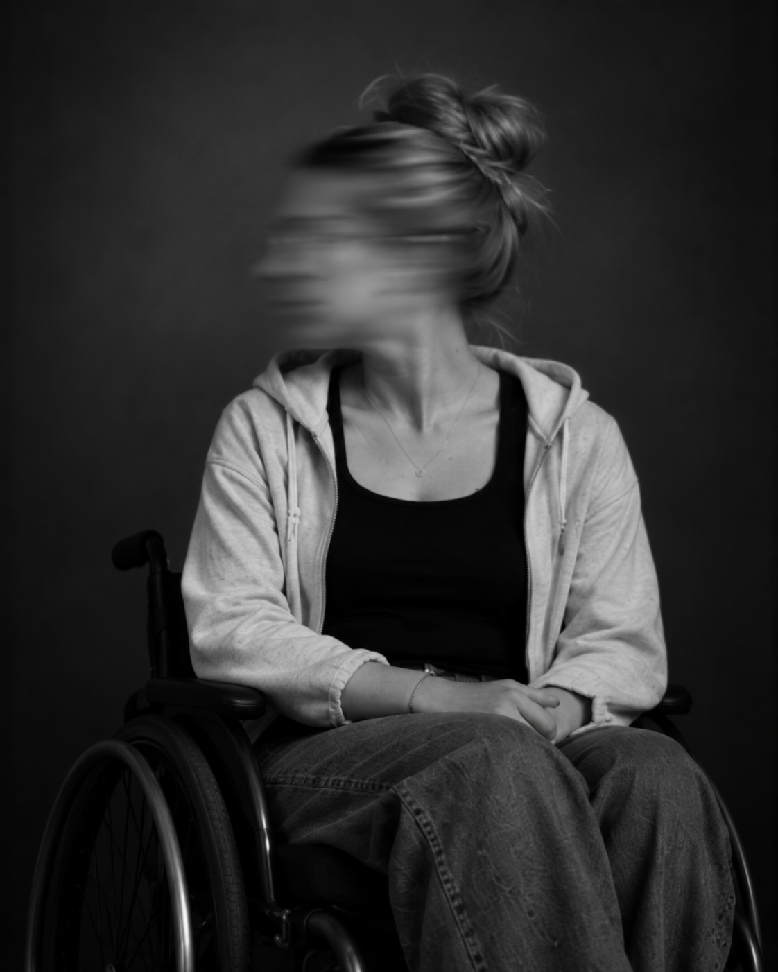 Sitzende Person im Rollstuhl mit hochgebundenen Haaren, heller Jacke und dunkler Kleidung. Das zur Seite gedrehte Gesicht ist durch Bewegungsunschärfe verschwomme
