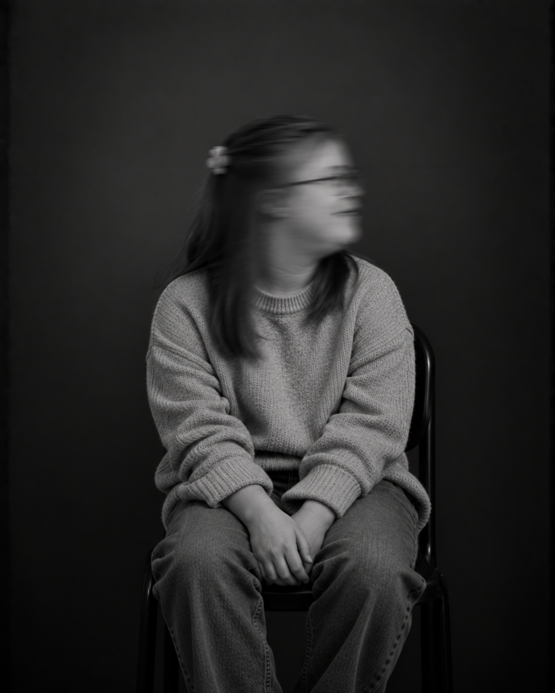 Sitzende Person mit langen Haaren und heller Kleidung, die beide Hände auf den Knien hält. Das zur Seite gedrehte Gesicht ist durch Bewegungsunschärfe verschwommen.