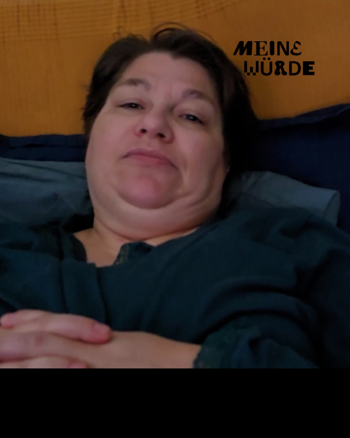 Person mit kurzen dunklen Haaren und dunklem Oberteil, liegend und frontal in die Kamera blickend. Rechts oben steht „Meine Würde“.